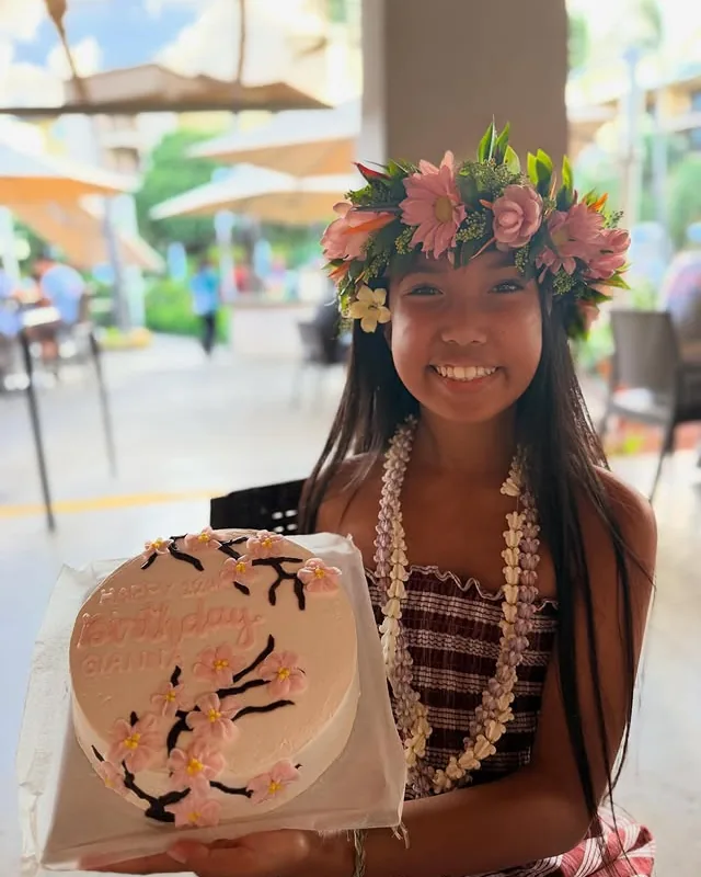 A Kauai Bakery team member in a haku lei holding a boxed custom cake